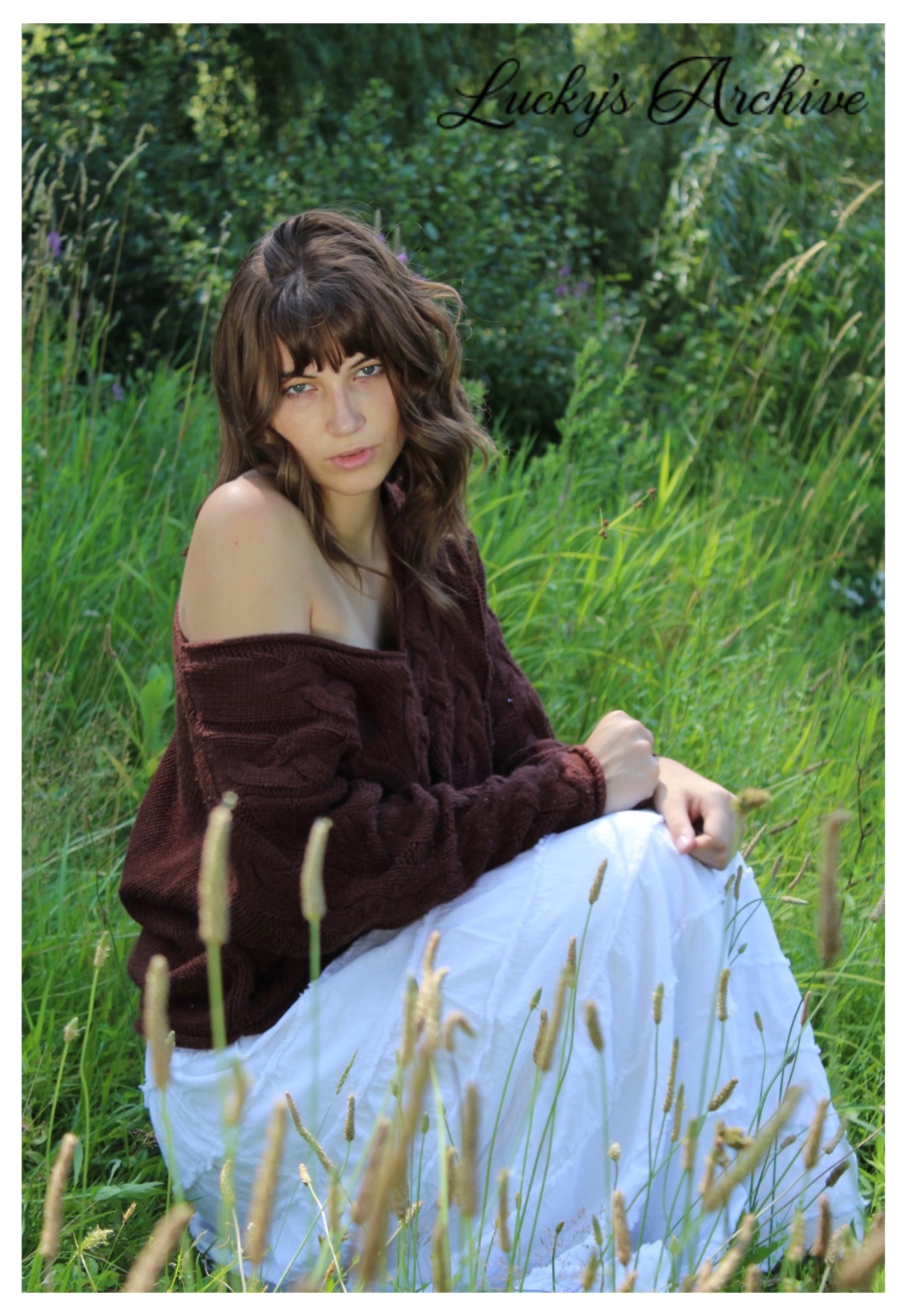 Portrait in a brown knit sweater seated in tall summer grass
