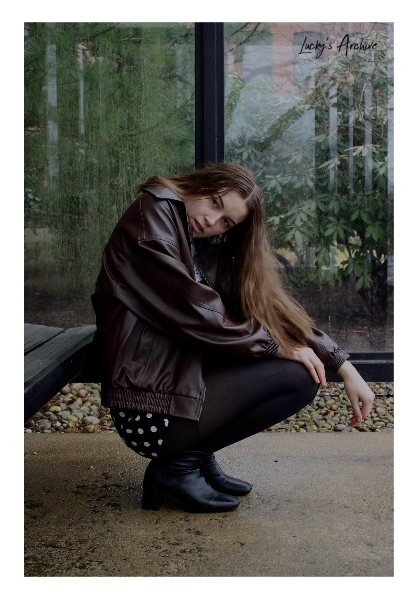 Editorial portrait in a leather jacket beside a glass shelter