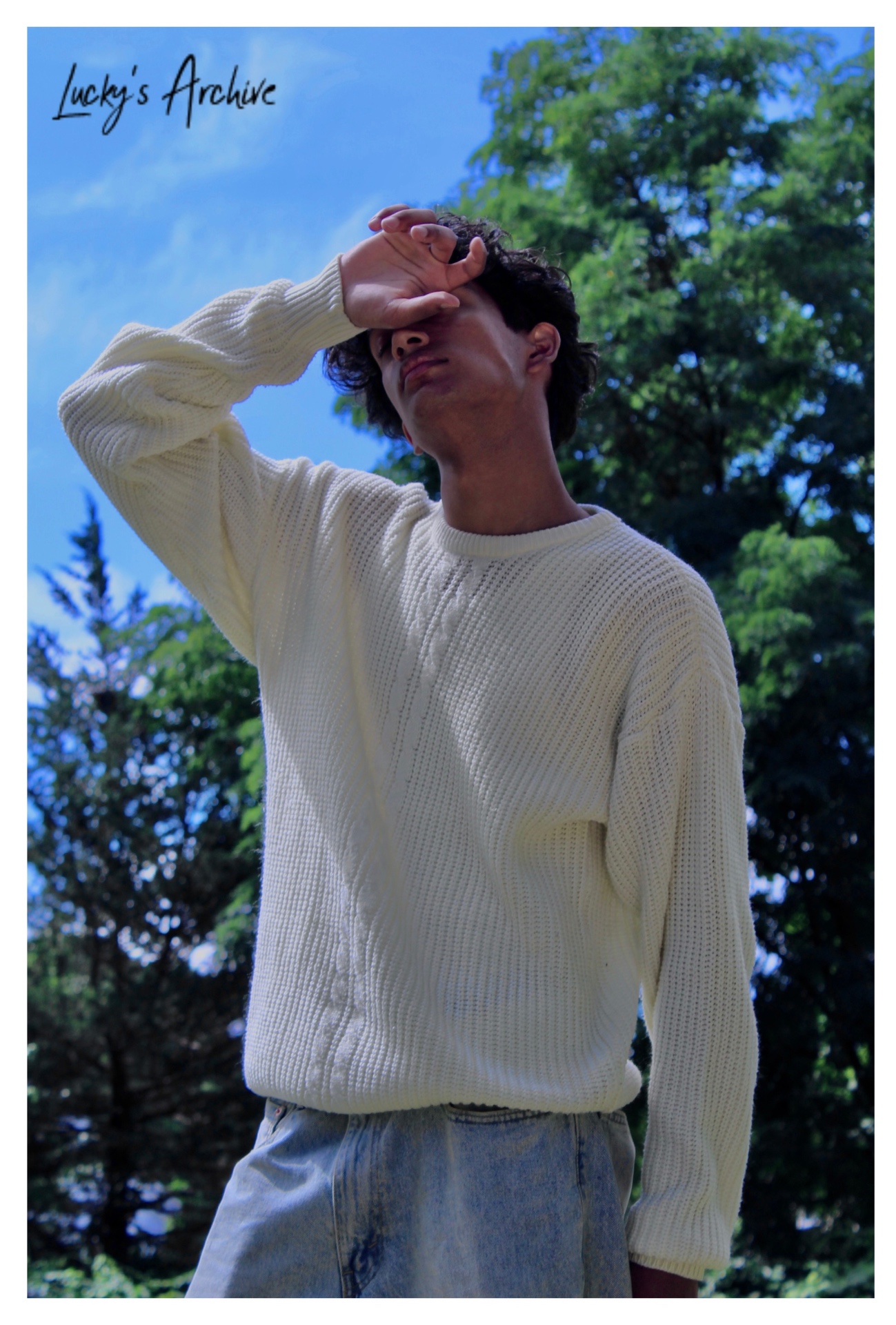 Low-angle portrait in a cream knit sweater against a blue sky